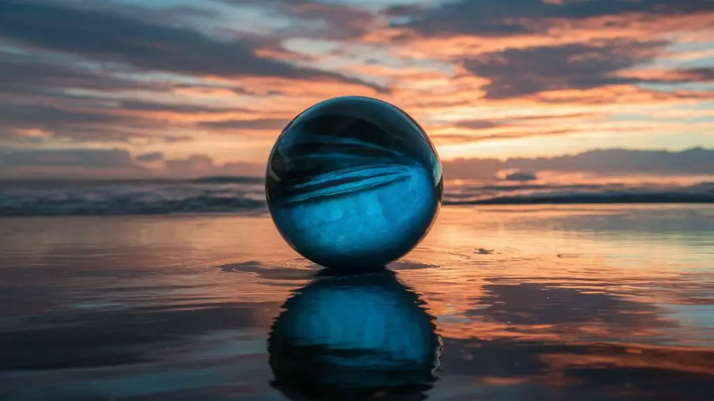 Blue glass sphere on reflective beach at sunset